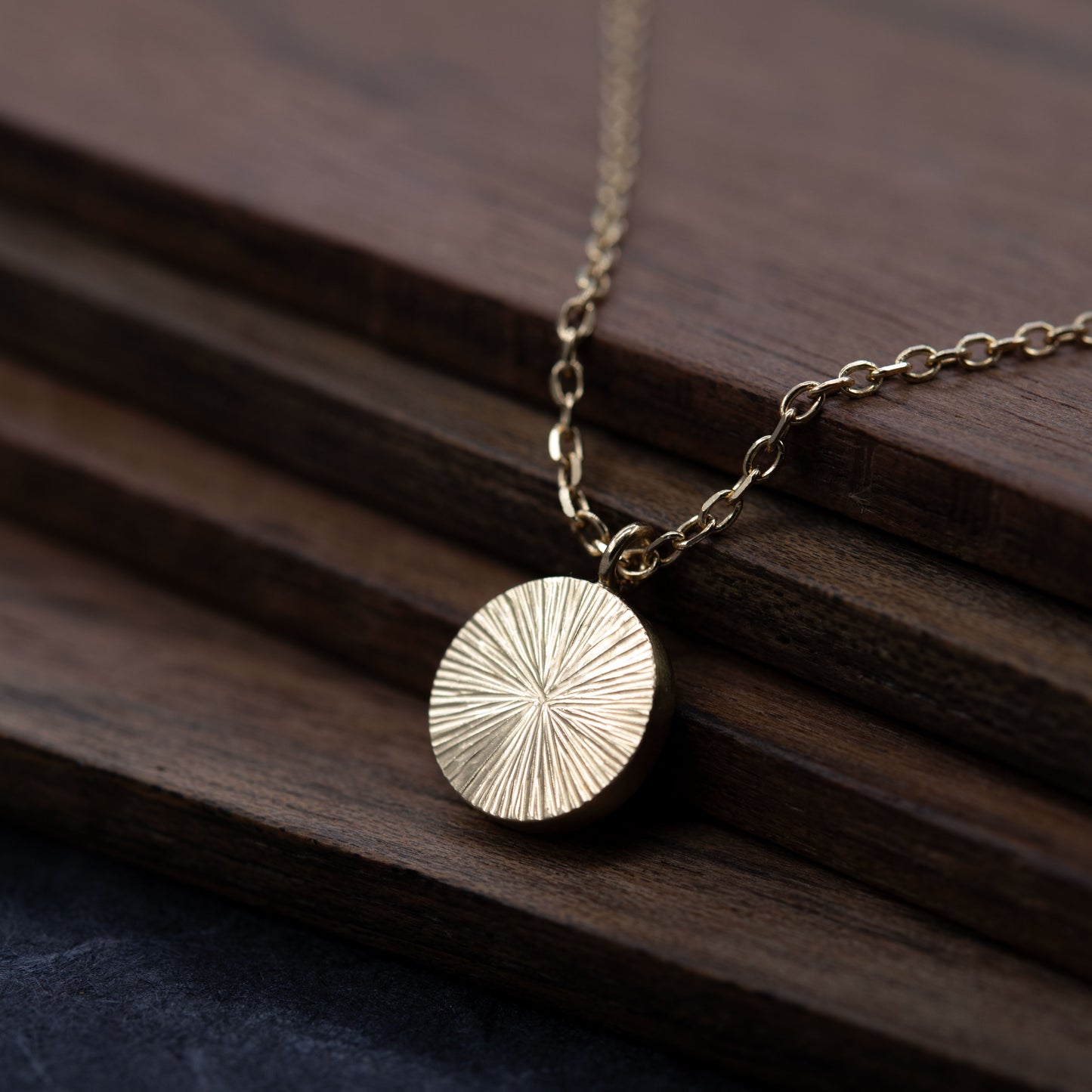 Front view of delicate gold vermeil necklace with a disc pendant on a wooden surface. Timeless minimalist jewelry made in Paris