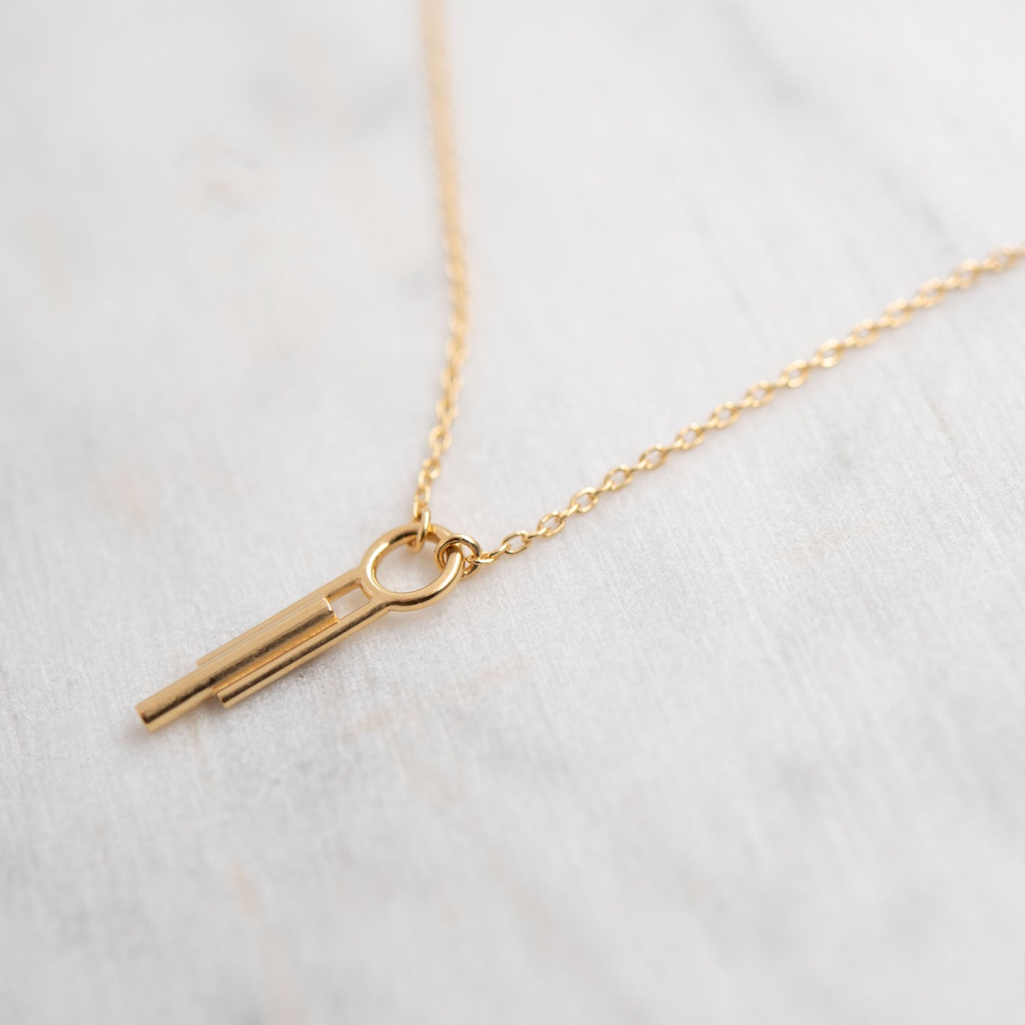 Detail of Art Deco cylinder pendant necklace on delicate cable chain against white marbre, minimalist handmade Paris jewelry
