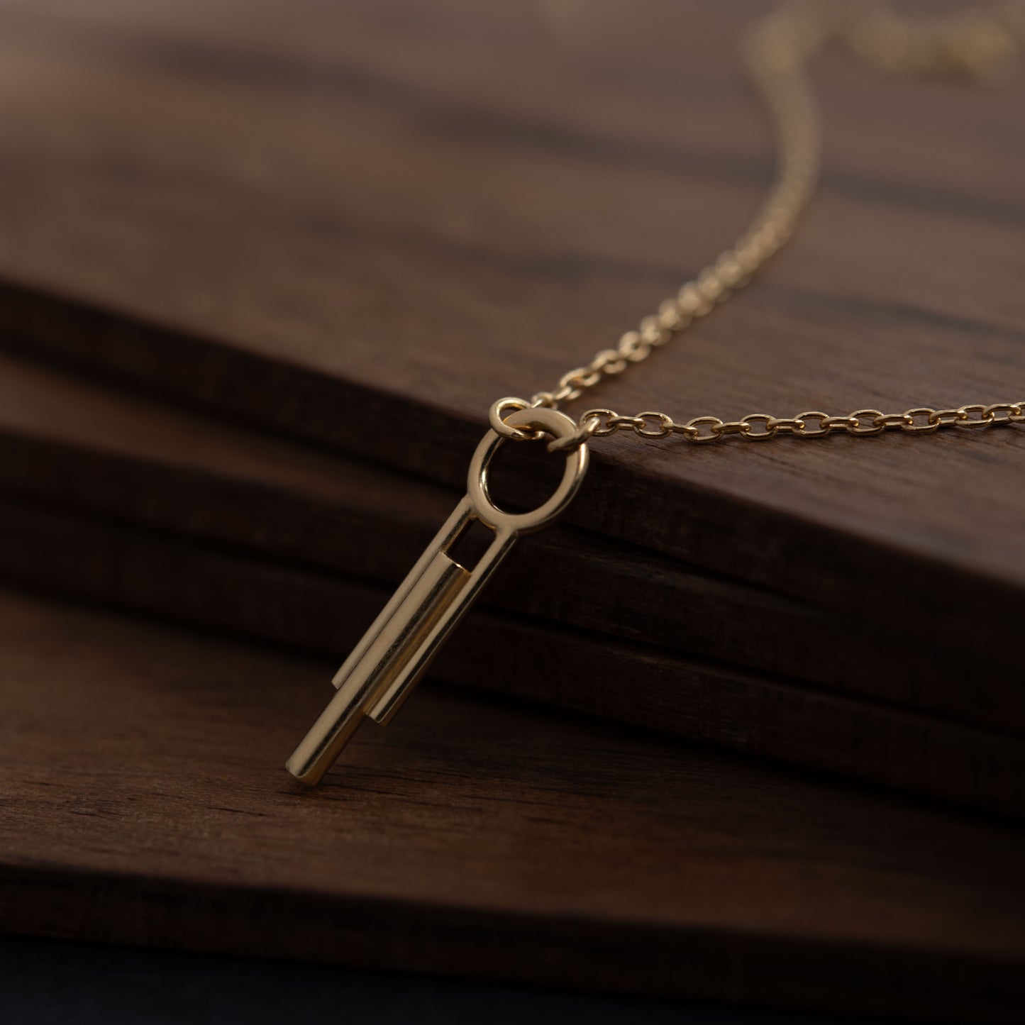 Close-up of Art Deco gold vermeil cylinder pendant on dark wood, minimalist handmade jewelry
