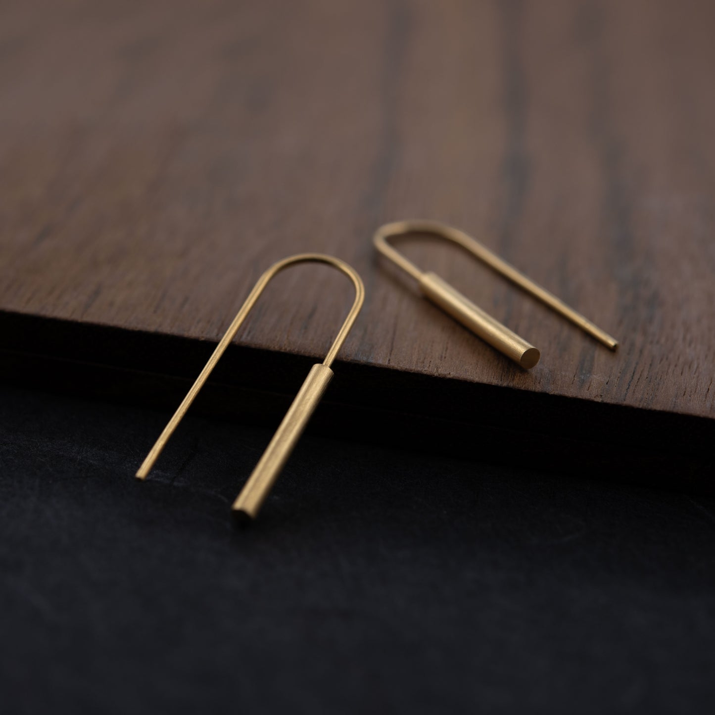 Boucles d’oreilles threader en vermeil posées sur surface en bois et fond sombre – design fin et minimaliste en argent plaqué or 24k, finition mate