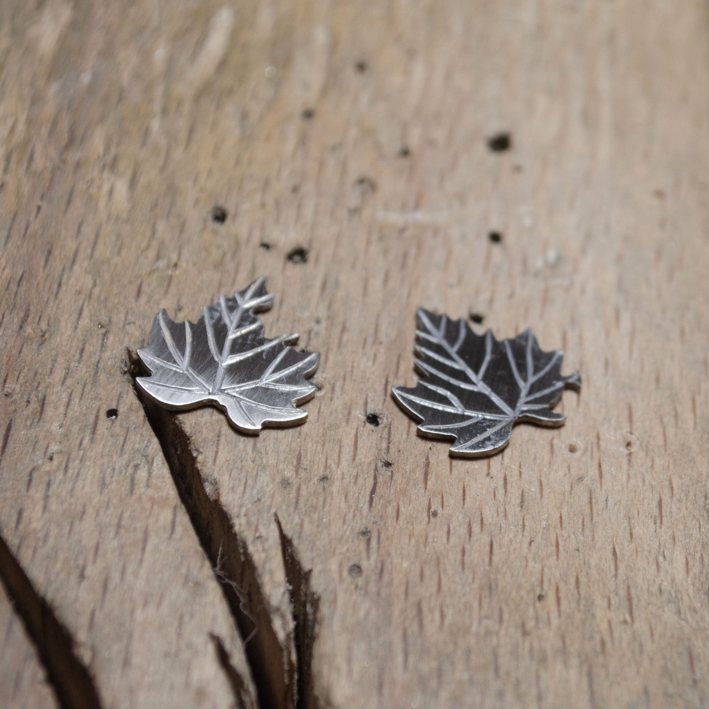 Close view of a silver leaf-shaped earrings on a wooden surface