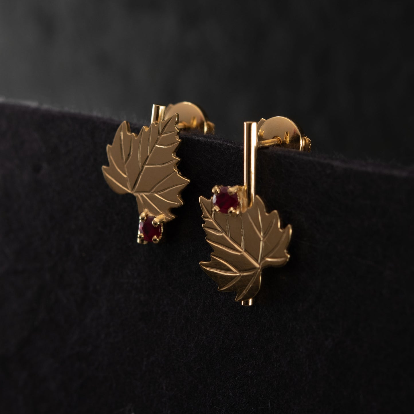 Gold leaf-shaped earrings with red gemstones on a black background