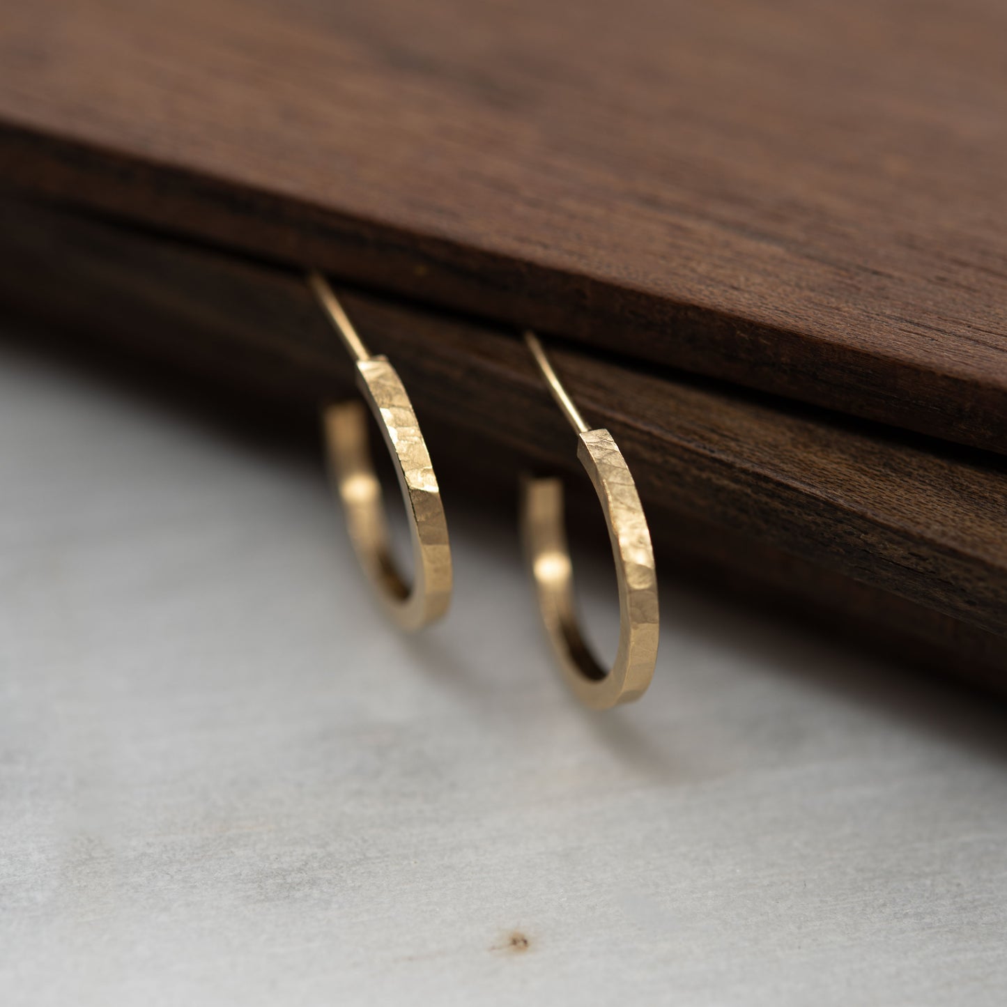 Hammered gold hoop earrings on a wooden surface.