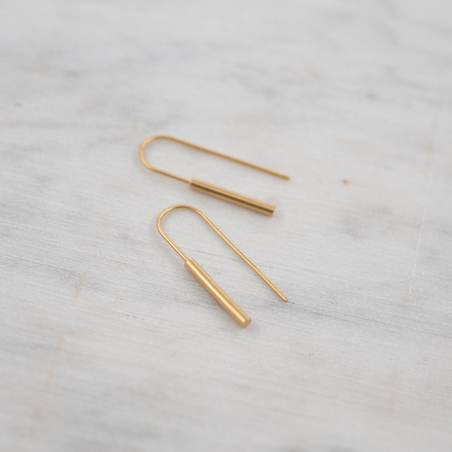 Pair of gold threader earrings in vermeil placed on a soft white marble background, minimalist handmade design in 24k gold-plated sterling silver with a matte finish