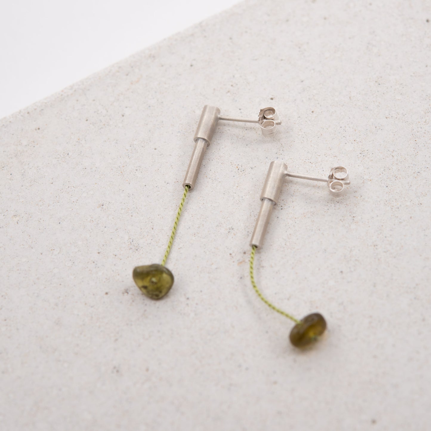 Pair of 37 millimeters length pendant earrings handmade in in Paris by A g J c from tube of matte sterling silver with a light green silk cord threaded through the center for hanging a green garnet stone.