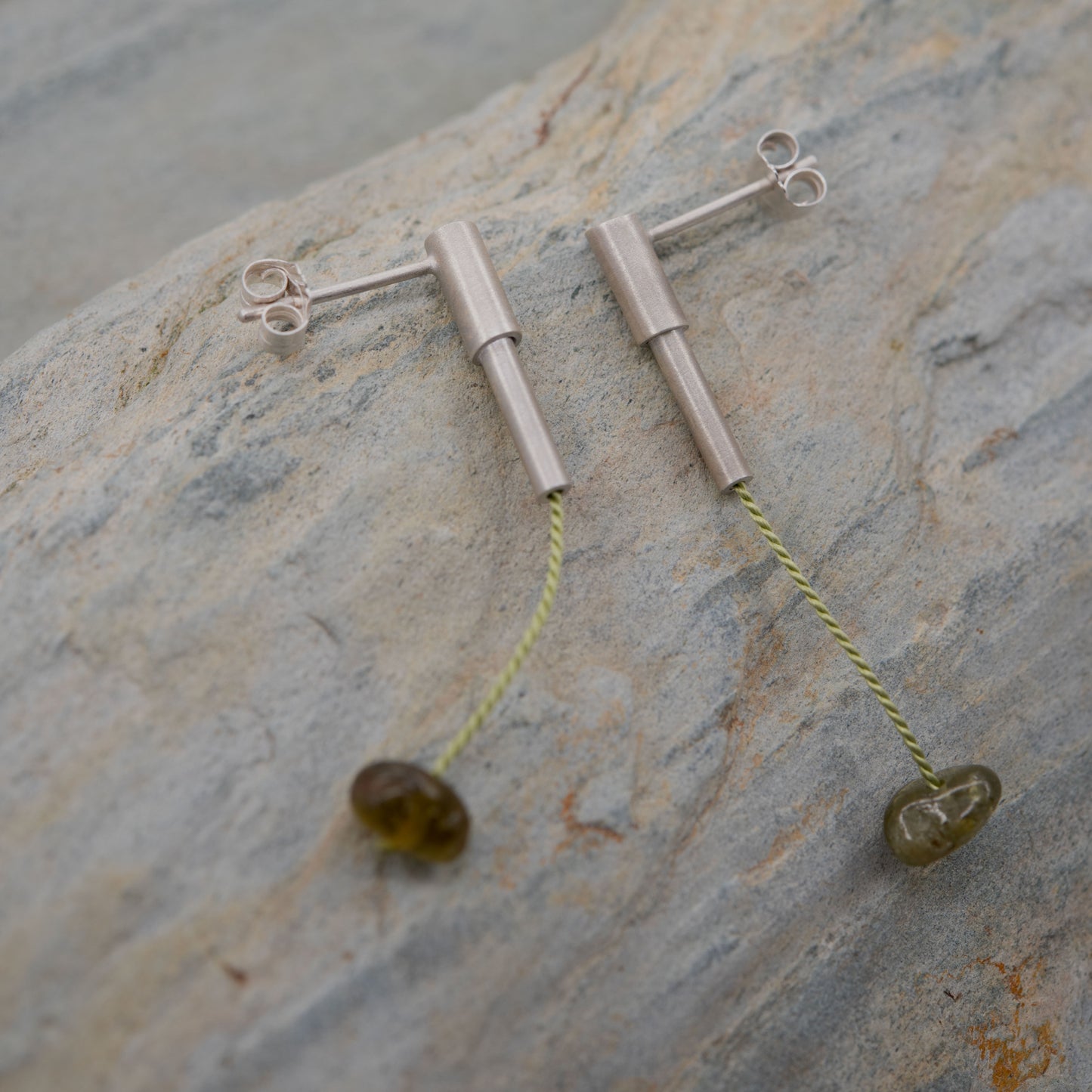 Pair of 37 millimeters length pendant earrings handmade in in Paris by A g J c from tube of matte sterling silver with a light green silk cord threaded through the center for hanging a green garnet stone.