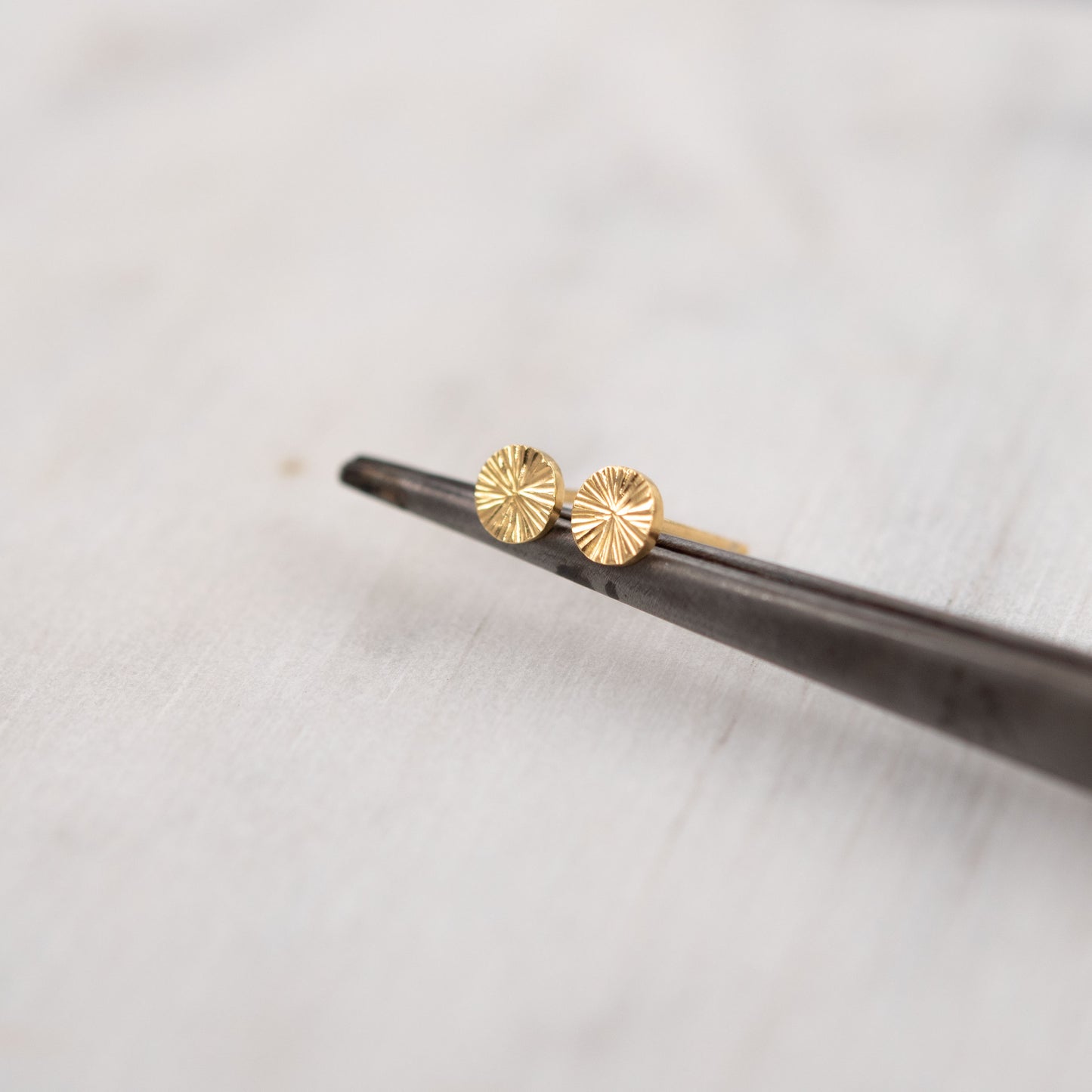 Gros plan de petites boucles d’oreilles clous en vermeil or gravé sur fond blanc – bijou talisman minimaliste de Paris