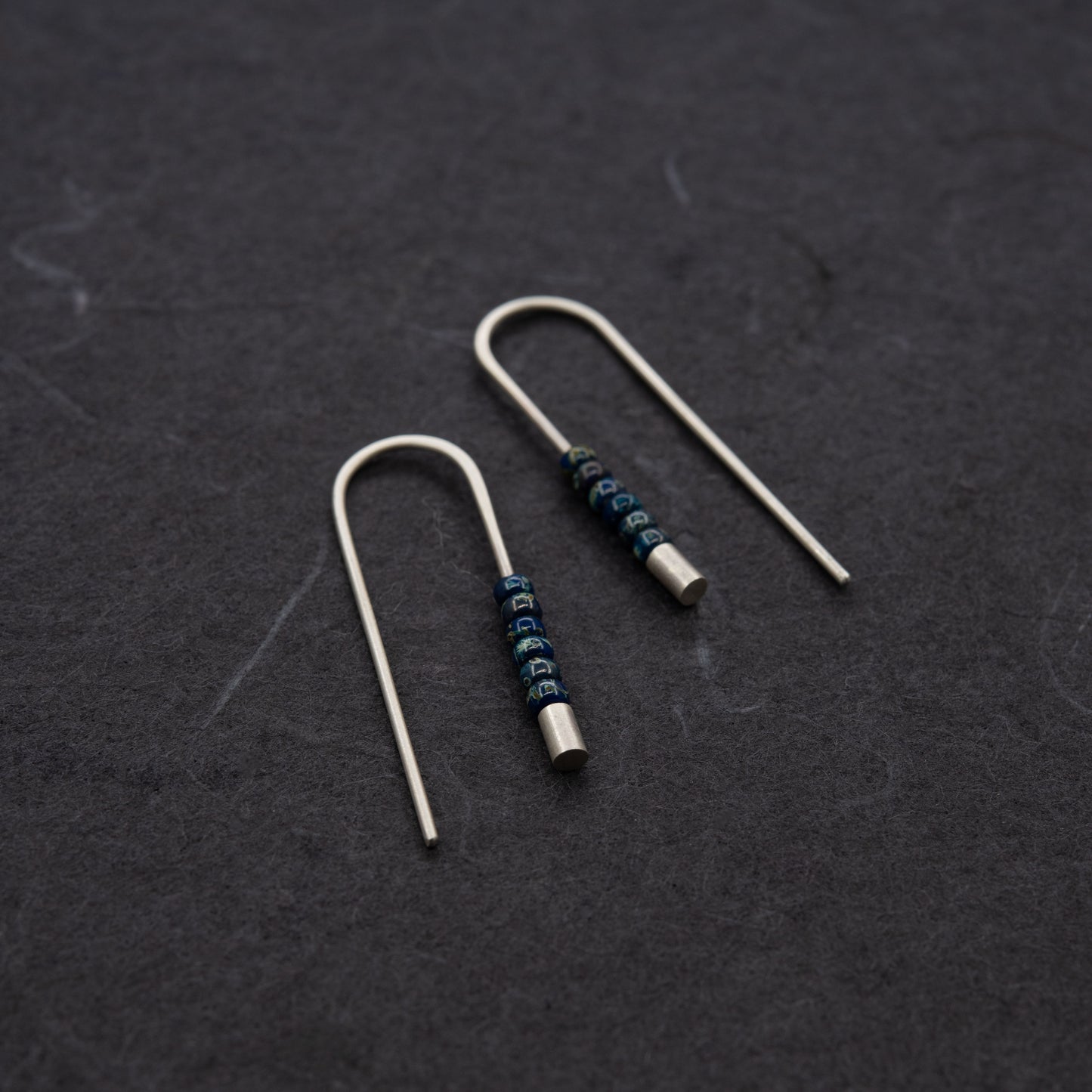 Gros plan sur des boucles d’oreilles en argent massif finition mate avec petites perles Miyuki bleues.