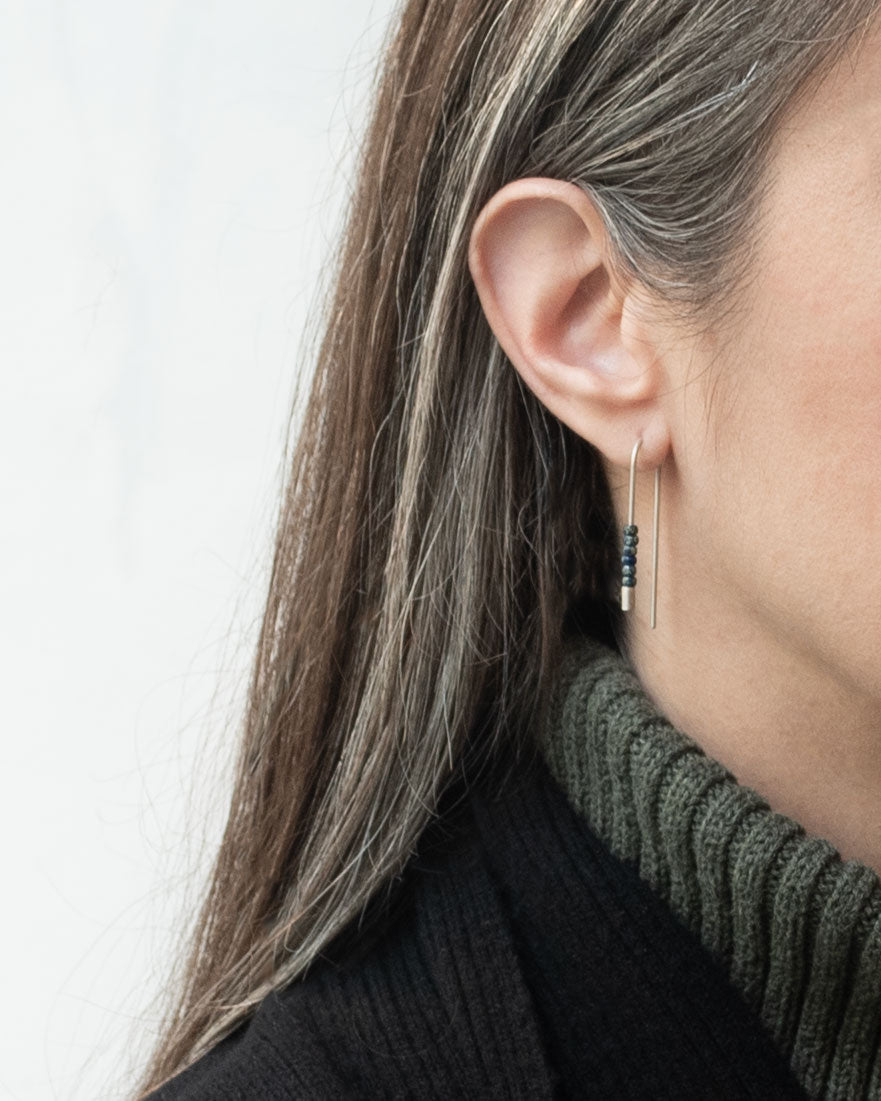 Femme portant des boucles d’oreilles fil en argent sterling avec perles Miyuki bleues, bijou élégant du quotidien.