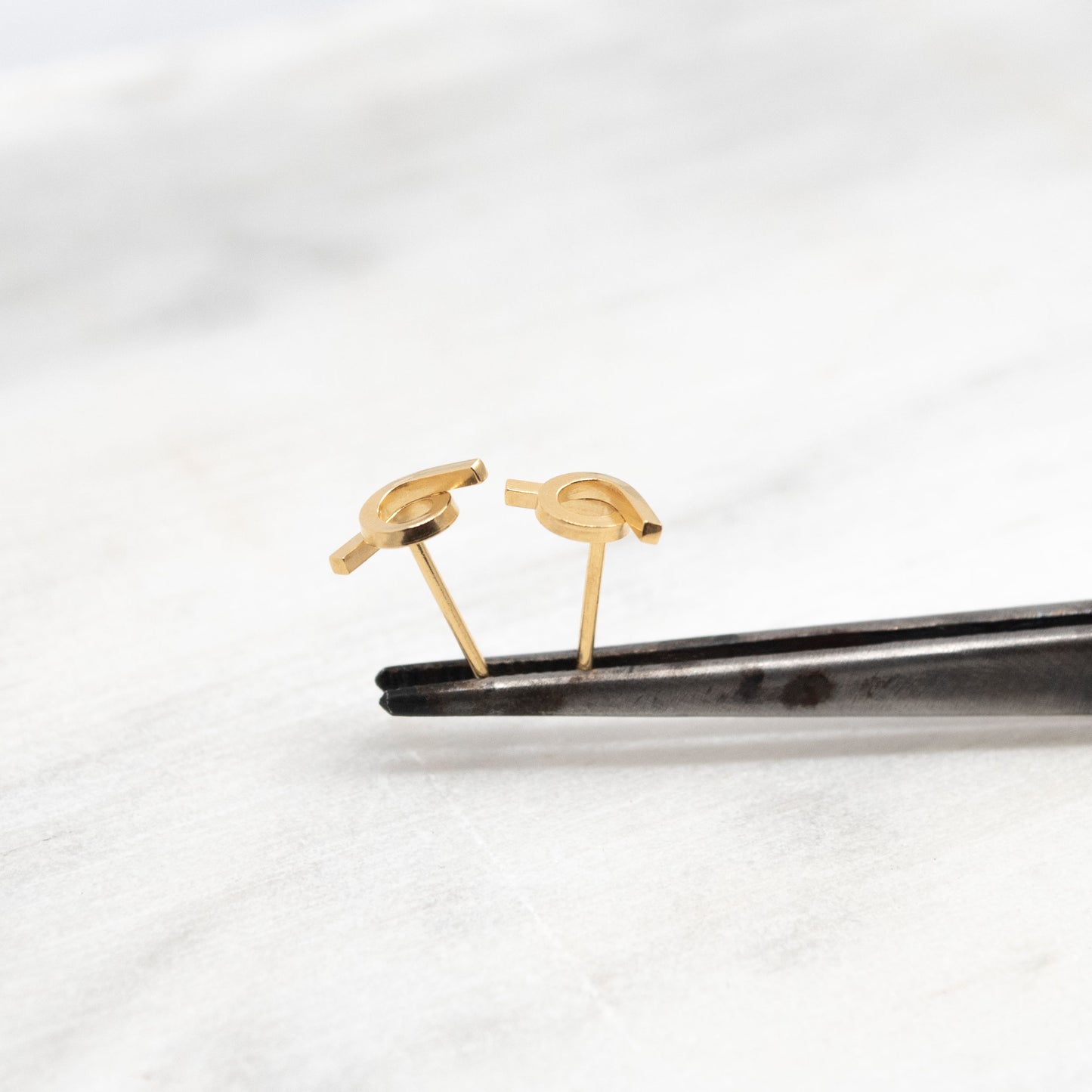 Vue rapprochée d'une paire de boucles d'oreilles en vermeil, posées sur une pince. Les boucles d'oreilles présentent un design entrelacé avec une finition brillante, mettant en valeur leur style moderne et minimaliste.
