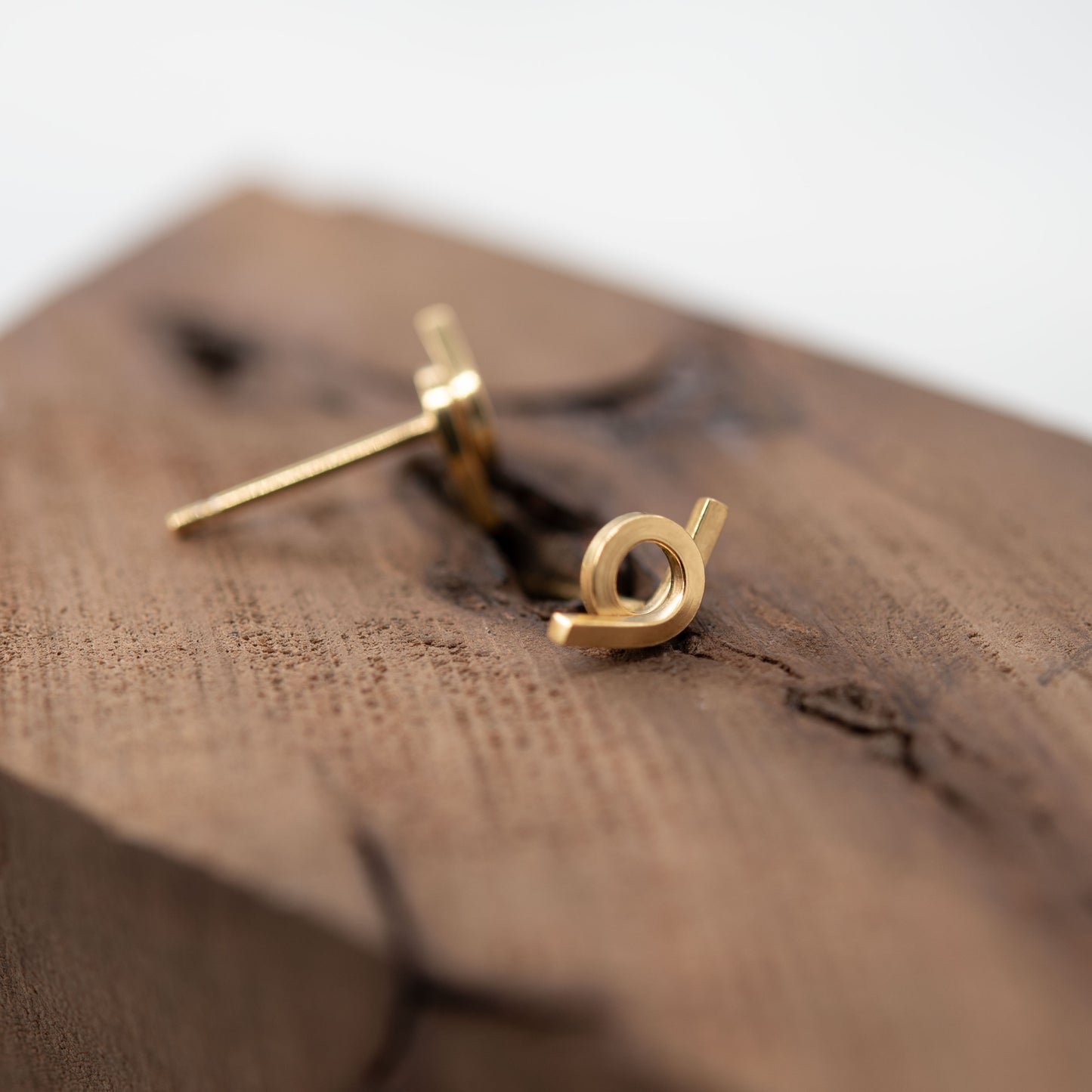 Vue en perspective d'une paire de boucles d'oreilles en vermeil avec un design entrelacé, posées sur une surface en bois texturé. L'image montre les tiges des boucles d'oreilles, mettant en avant leur finition brillante et leur style moderne.