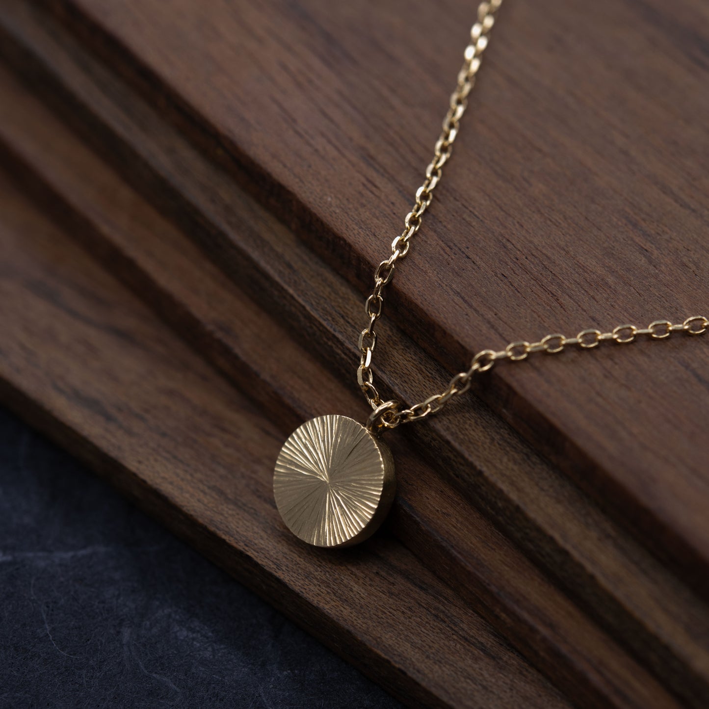 Gros plan sur bois foncé collier médaille texturée en vermeil or, idée cadeau artisanale unique fait àParis.