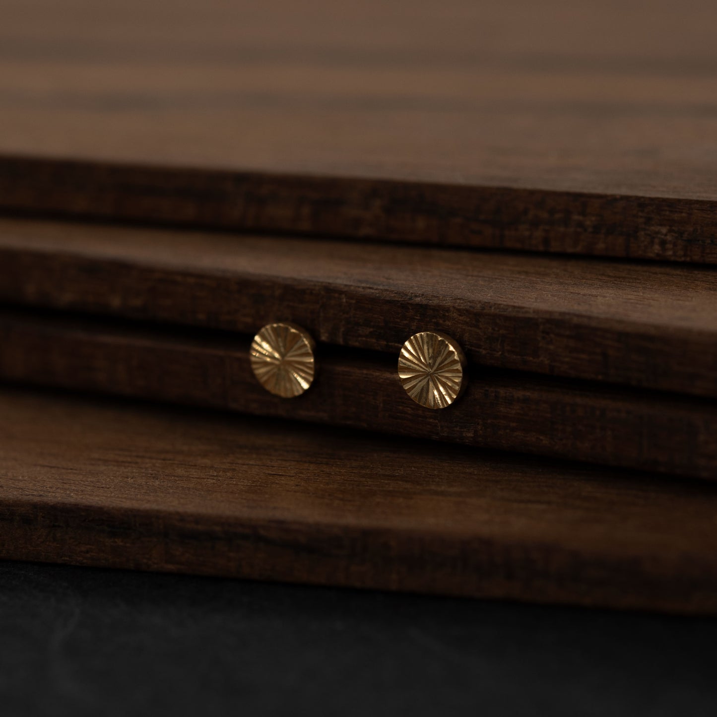 Vue de côté de boucles d’oreilles médaille en vermeil doré gravé posées sur bois – bijou artisanal parisien