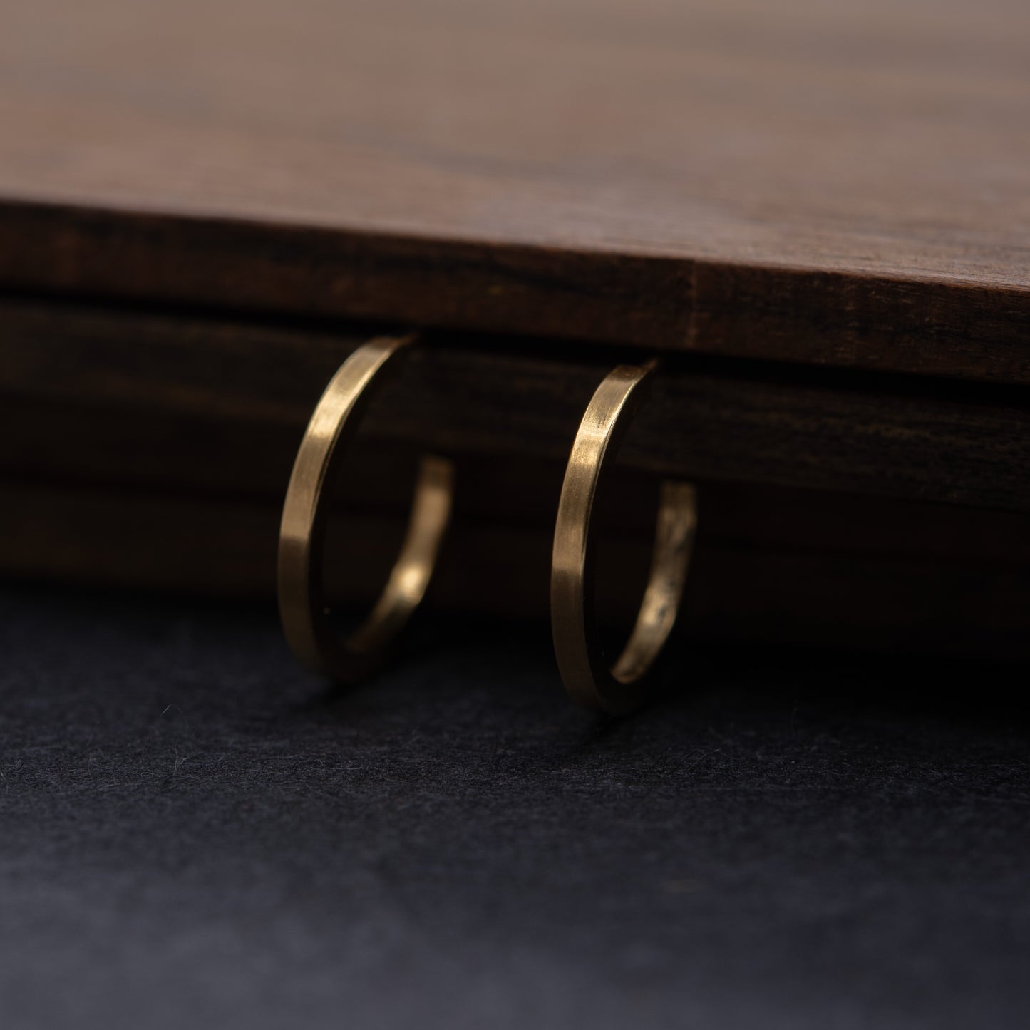 Pair of gold vermeil hoops hanging on a wooden surface, minimalist 24k gold-plated jewelry.