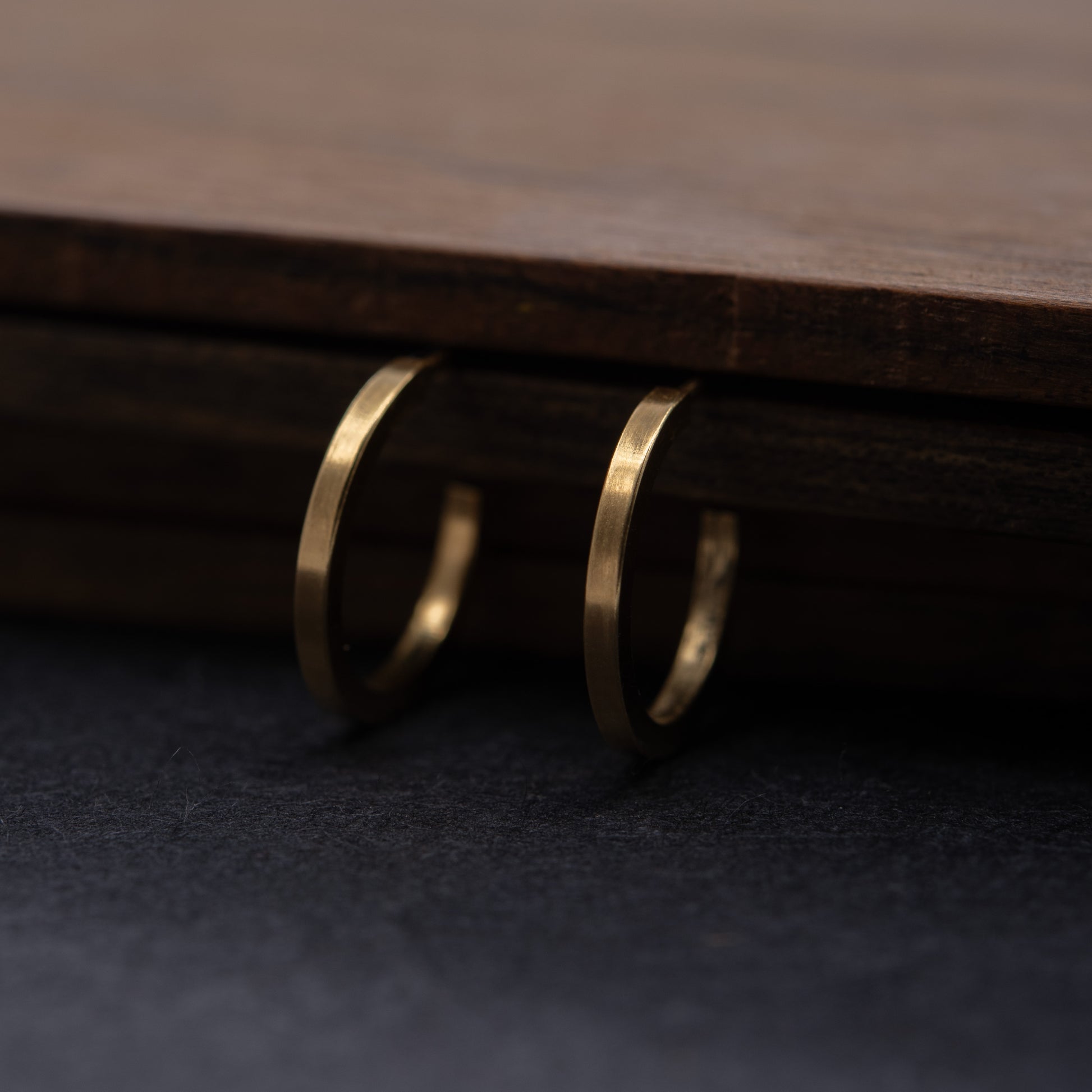 Pair of gold vermeil hoops hanging on a wooden surface, minimalist 24k gold-plated jewelry.