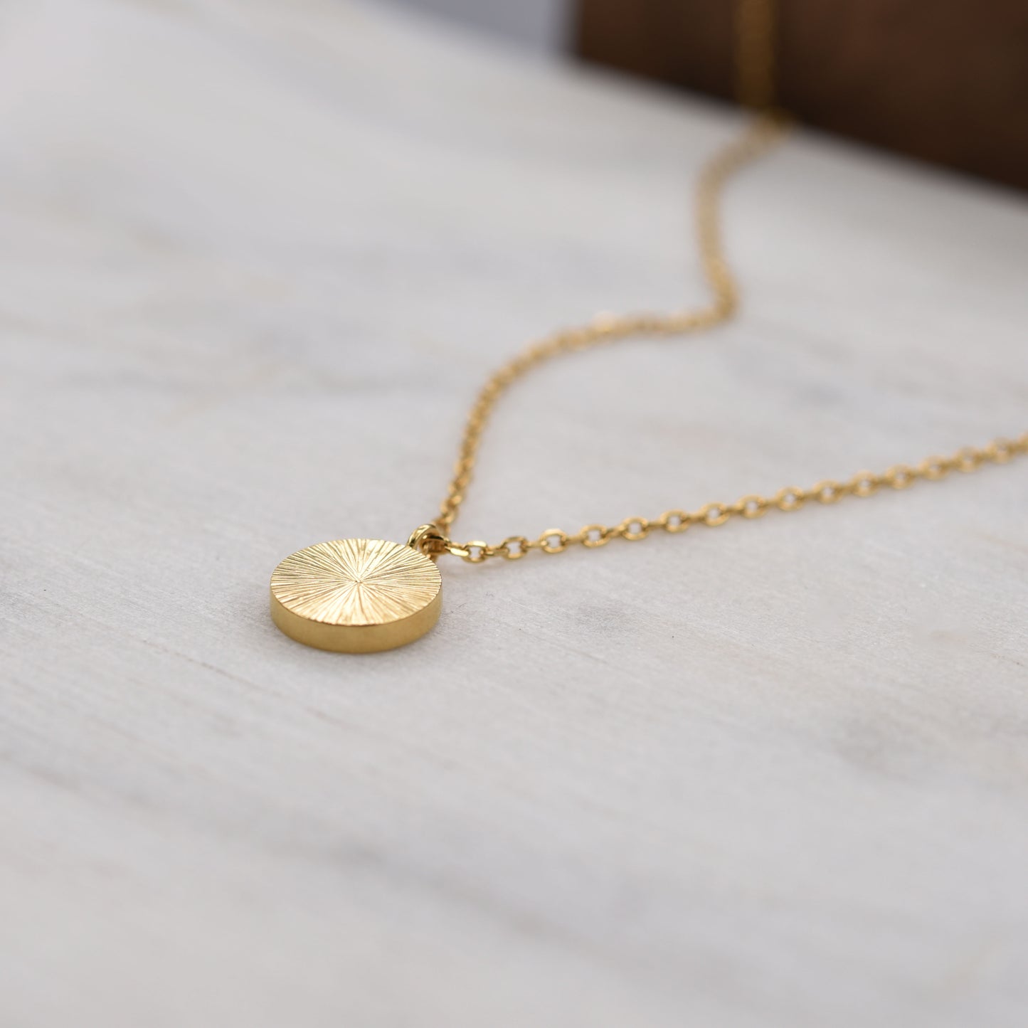 Side angle of gold vermeil sunburst pendant necklace, minimalist artisan jewelry from Paris.