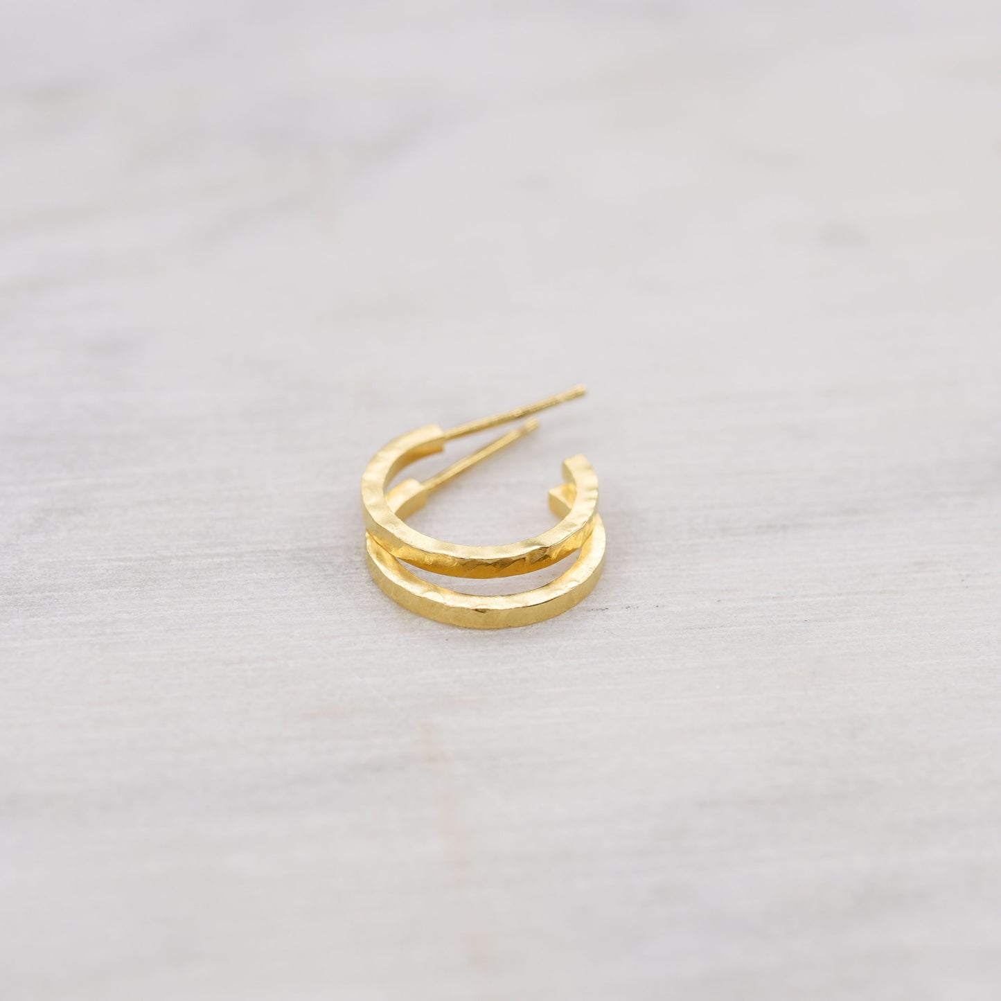 hammered gold hoop earrings on a light marbre background