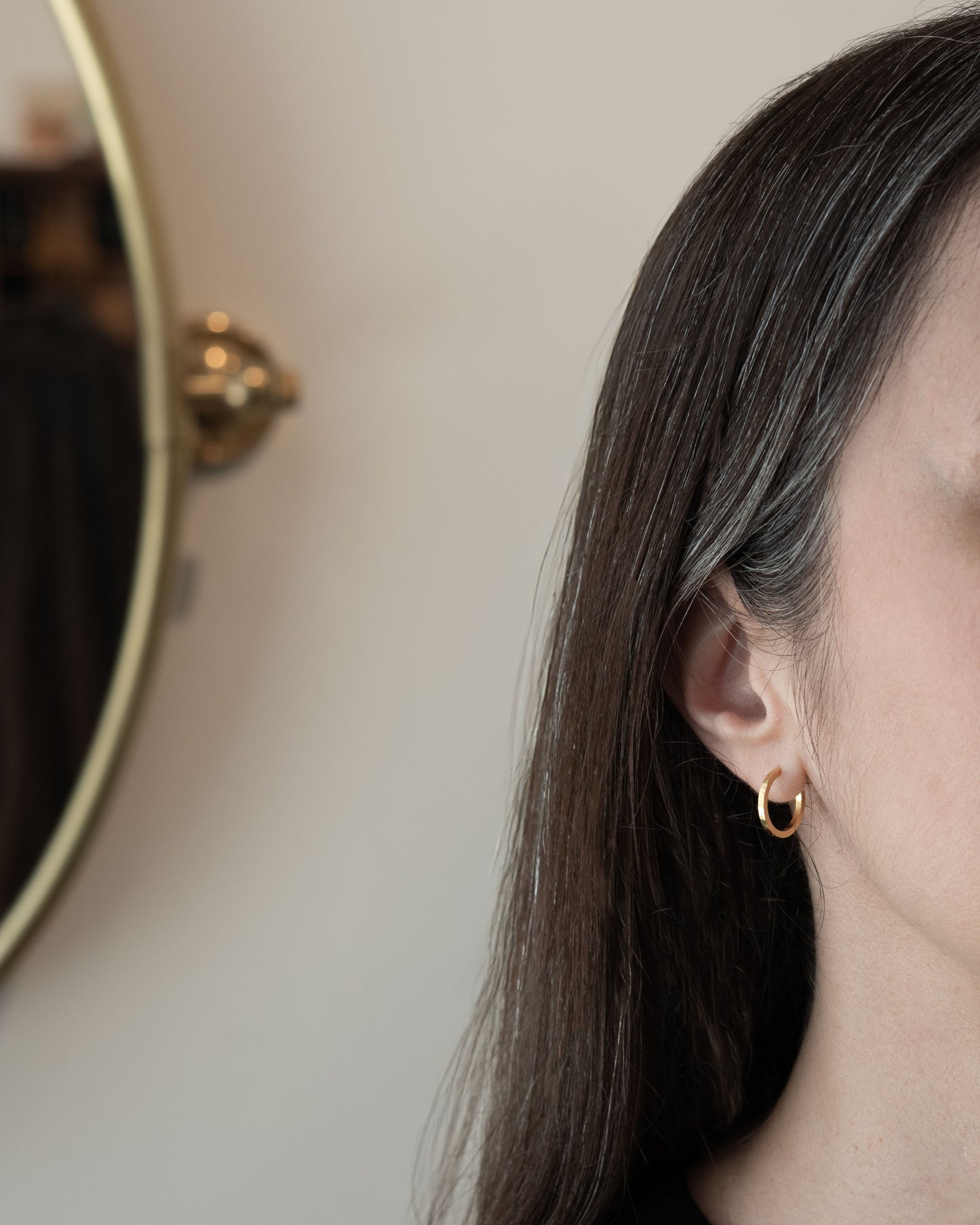 Gros plan sur une personne portant une boucle d'oreille créole en or avec un fond neutre