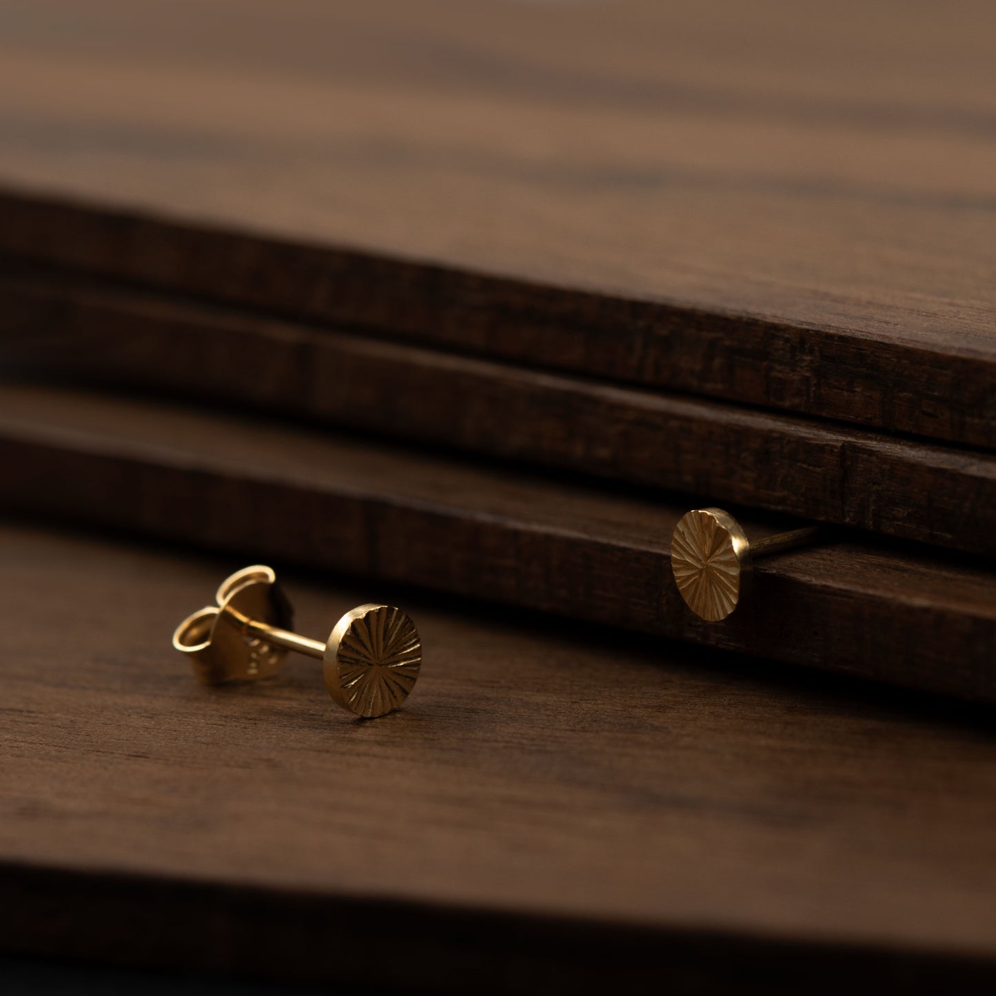Detailed close-up of engraved gold vermeil stud earrings on dark wood – modern Paris artisan jewelry design