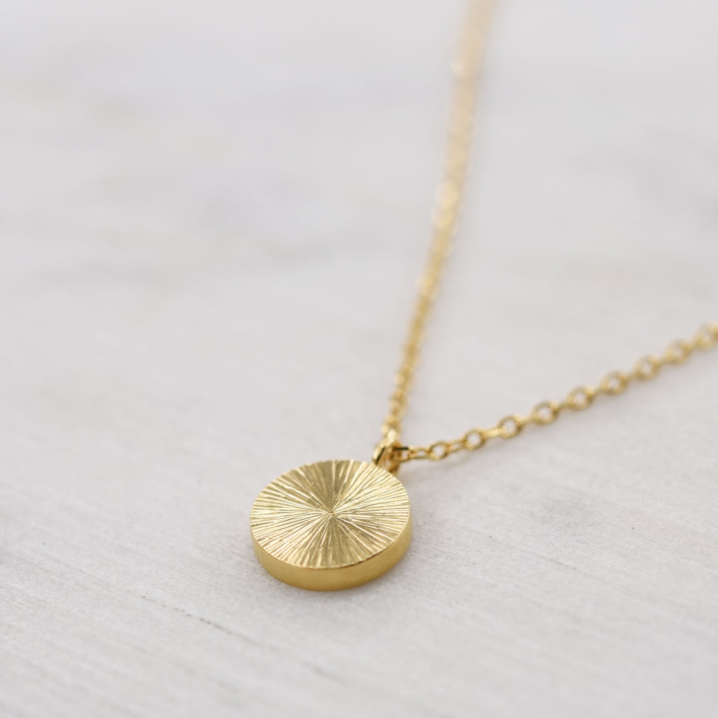 Close-up of textured gold vermeil medallion necklace on a light gray background, unique artisan jewelry gift idea.