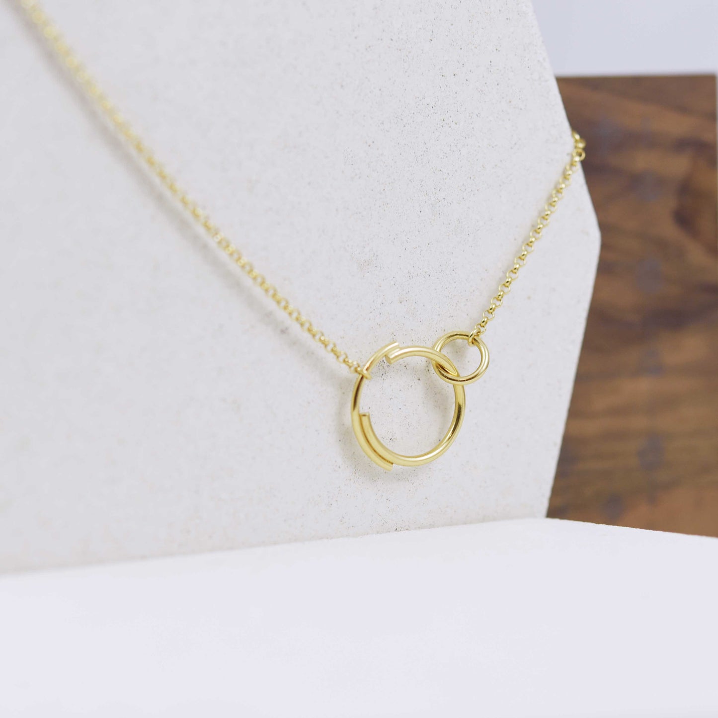 A close up of a stylish interlocking circle necklace in gold that features a small circle clasping onto a larger circle that is made up of two separate arcs for a truly eclectic design.