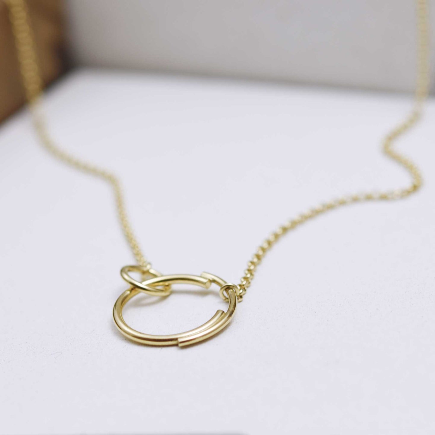 A close up of a stylish interlocking circle necklace  in gold that features a small circle clasping onto a larger circle that is made up of two separate arcs for a truly eclectic design.