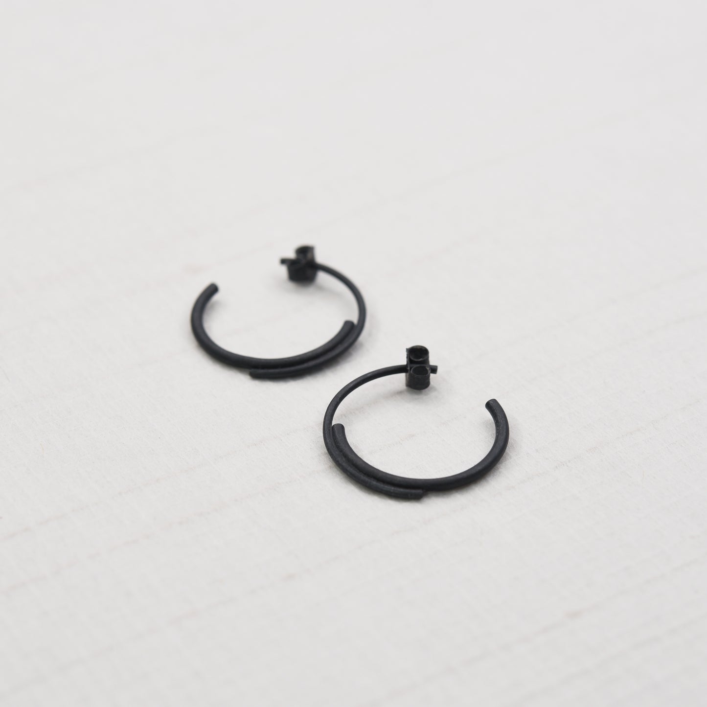 close up of a concentric circle small pair of hoops earrings in black oxidized silver in a white background