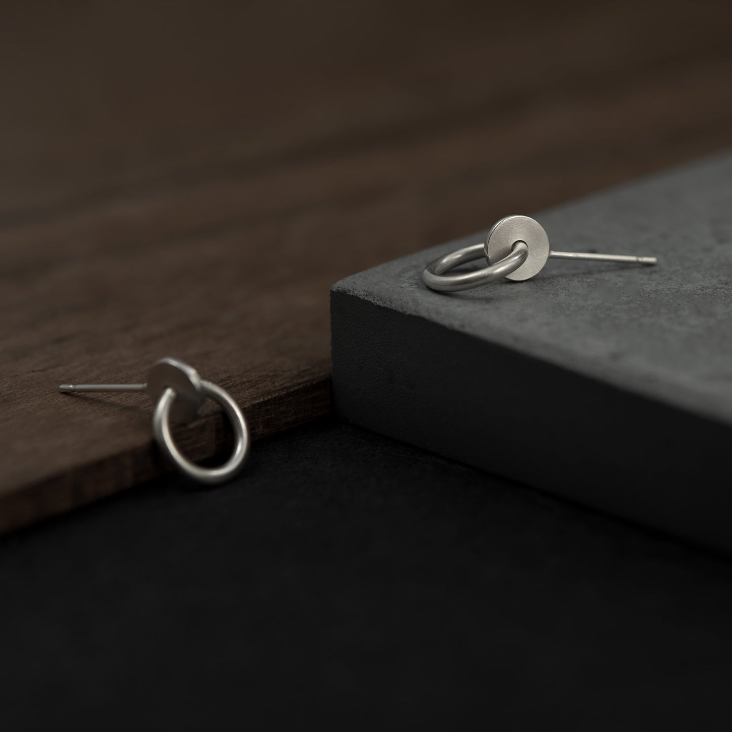 Close up of a pair of silver matte studs designed with an interlocked dot and circle The earrings measure 13 millimeters in length.