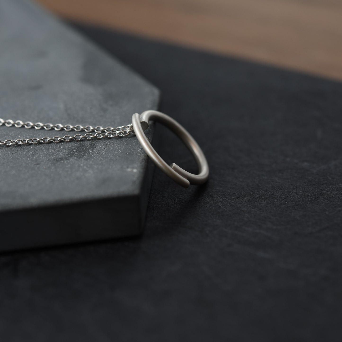 A dark blue background showing a close up of a 22 millimetres diameter circle pendant necklace handmade in silver brush matte finished