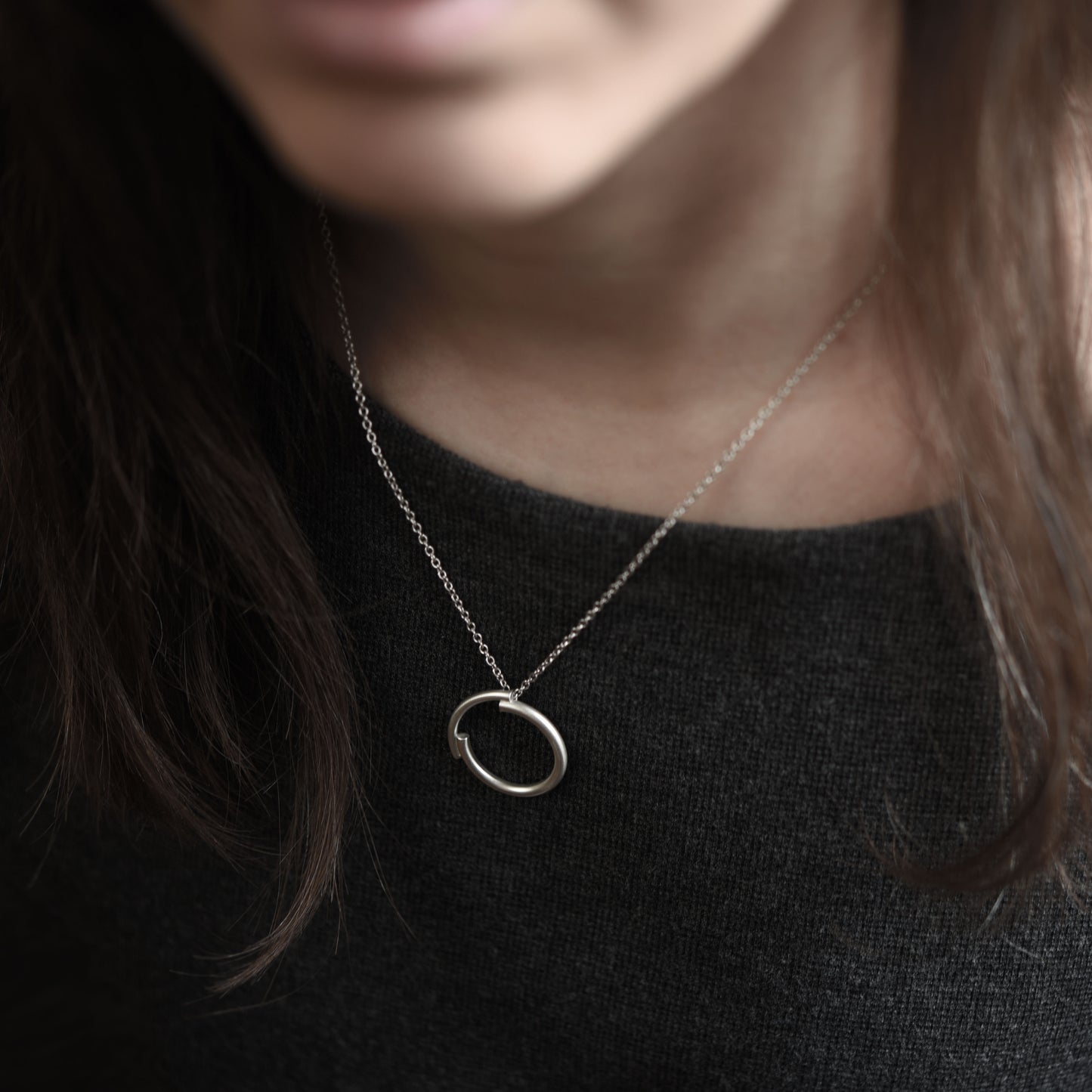 A close up of a chestnut brown hair woman wearing a 22 millimetres diameter circle pendant necklace handmade in silver brush matte finished