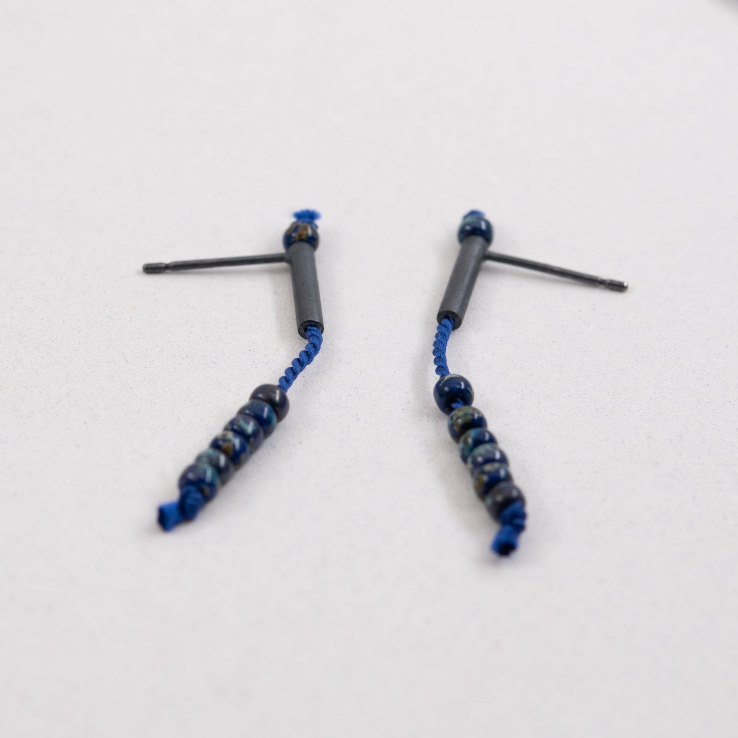 Pair of 38 mm length pendant earrings handmade in oxidized black sterling silver tube with a blue silk cord threaded through the center for hanging Picasso blue Miyuki beads. Designed and made by hand in Paris by A g J c