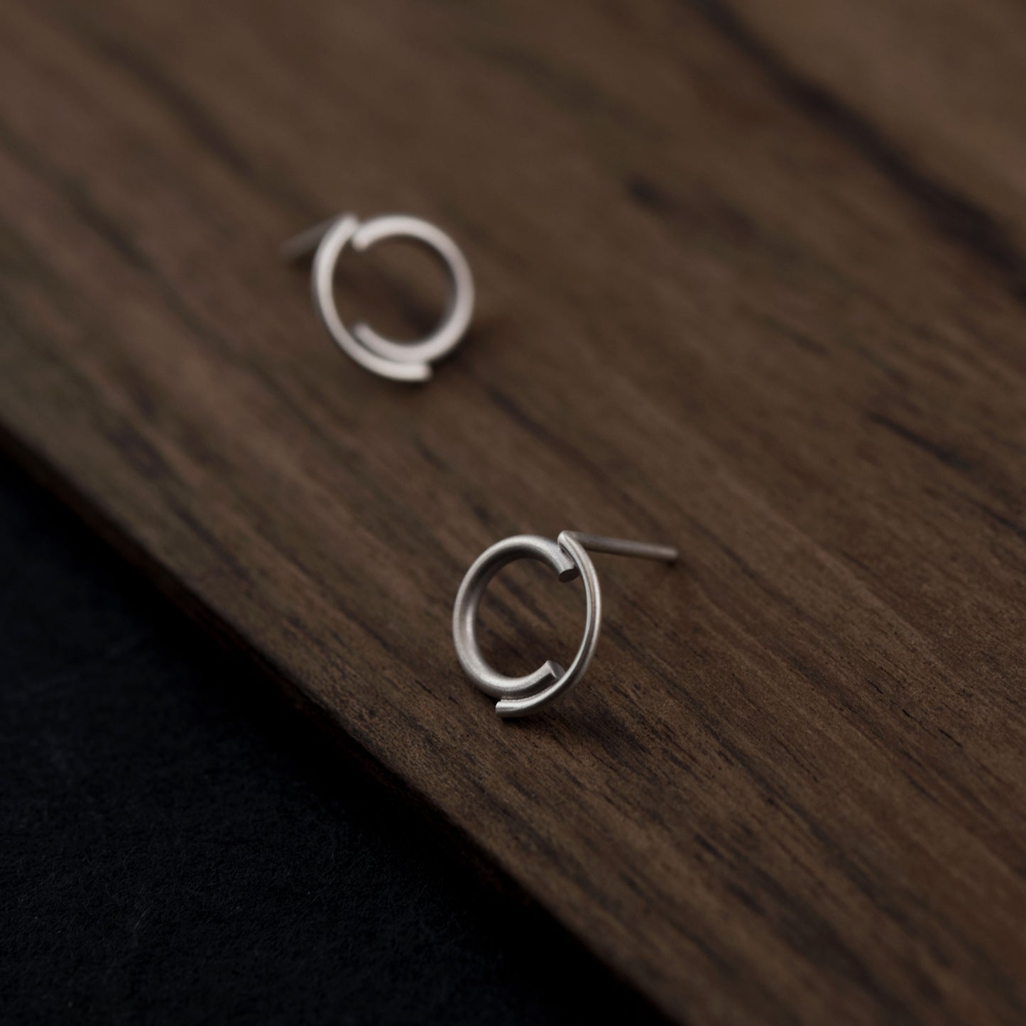 A close up of a concentric circle minimalist silver studs matte finished with a dark wood background
