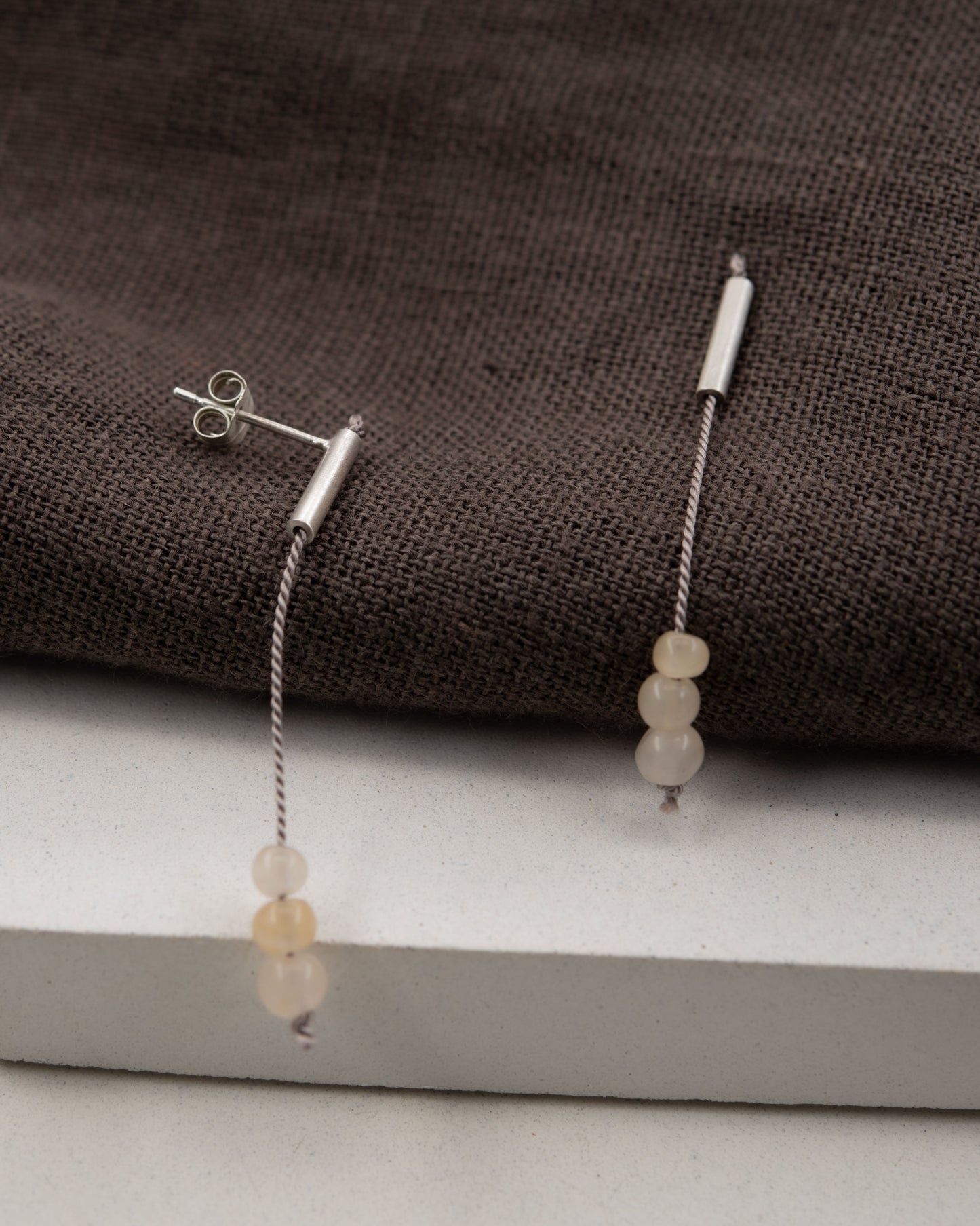 Pair of 42 millimeters length pendant earrings handmade in in Paris by A g J c  from  tube of matte sterling silver with a beige silk cord threaded through the center for hanging yellow quartz beads. 