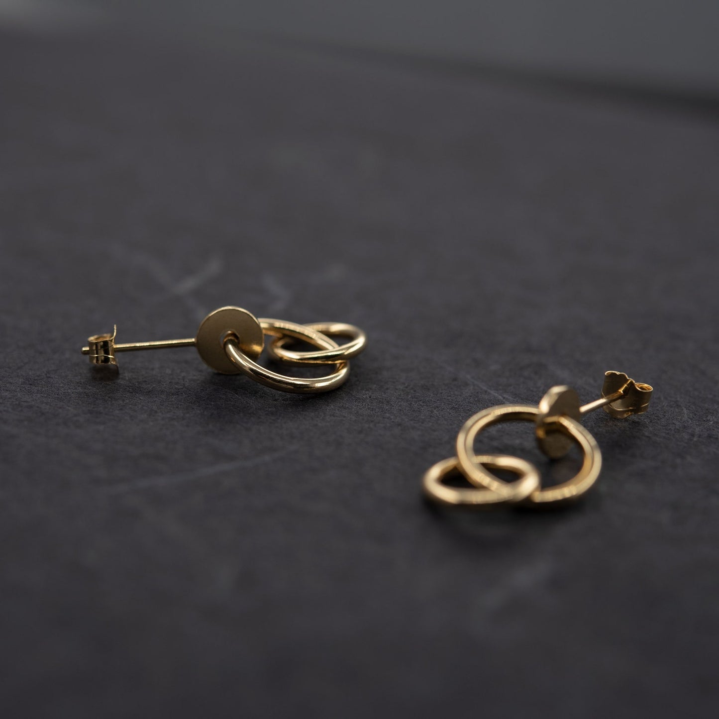 Pair of gold plated studs earrings designed with an interlocking dot and two hoops linked in shiny finish. Handcrafted by a g j c in Paris. The drop length measures 19 millimeters with a total earrings length of 22 millimeters. They can be worn on the ear lobe and attached with push backs.