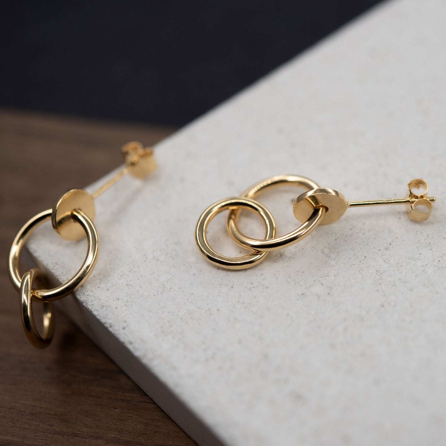 Pair of gold plated studs earrings designed with an interlocking dot and two hoops linked in shiny finish. Handcrafted by a g j c in Paris. The drop length measures 19 millimeters with a total earrings length of 22 millimeters. They can be worn on the ear lobe and attached with push backs.