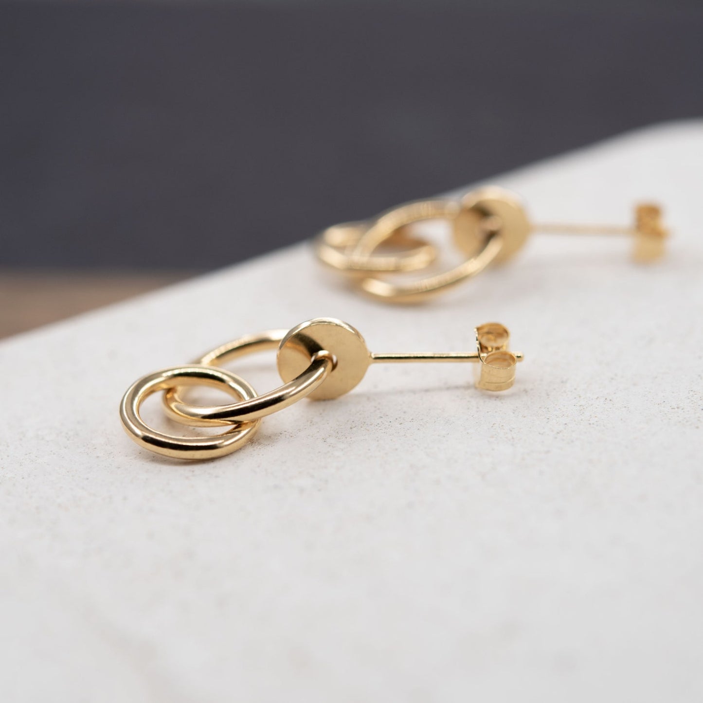 Pair of gold plated studs earrings designed with an interlocking dot and two hoops linked in shiny finish. Handcrafted by a g j c in Paris. The drop length measures 19 millimeters with a total earrings length of 22 millimeters. They can be worn on the ear lobe and attached with push backs.