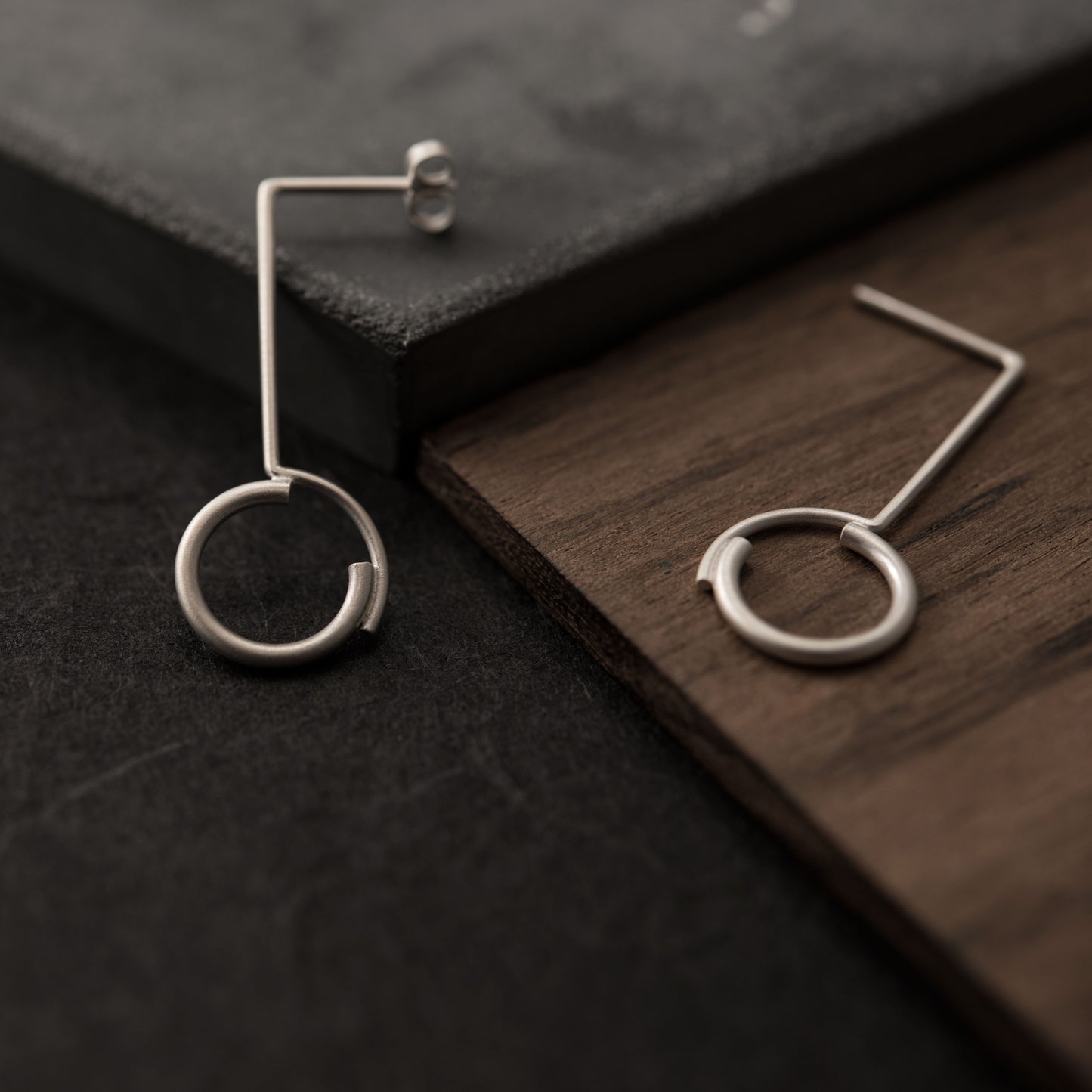 A close up of a pair of sterling silver earrings of 32 millimeters in height in a dark backgroung