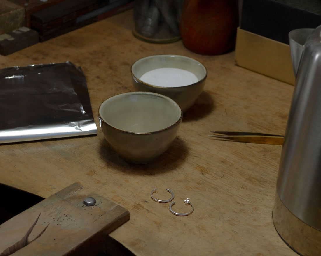 Jewelry workbench with tools, two bowls, aluminum foil, tweezers, and sterling silver earrings setup for cleaning silver.