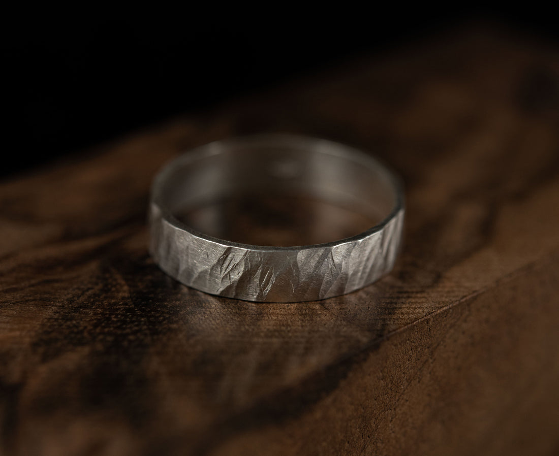 Minimalist handcrafted sterling silver ring with an engraved texture, photographed on a dark wooden surface.