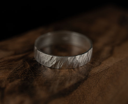Minimalist handcrafted sterling silver ring with an engraved texture, photographed on a dark wooden surface.