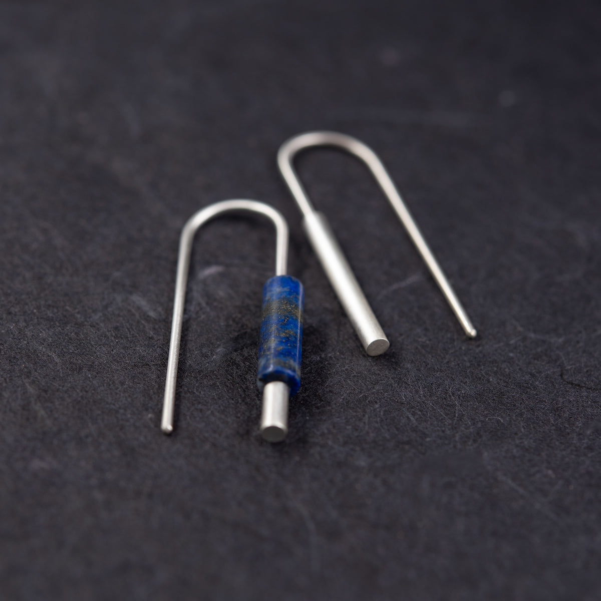 Boucles d’oreilles dépareillées en argent massif et lapis-lazuli bleu, vue rapprochée sur fond noir.