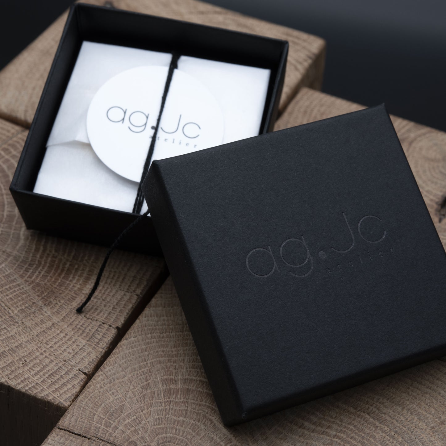 Black jewelry box with 'ag.Jc' branding on a wooden surface