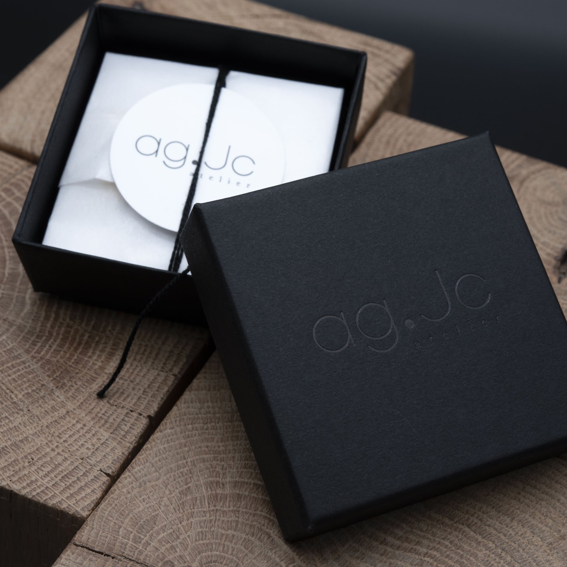 Black jewelry box with 'ag.Jc' branding on a wooden surface