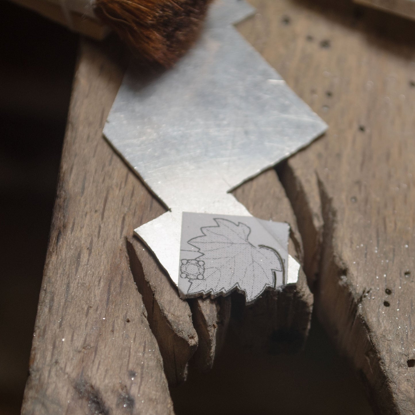 close view of a sterling silver stamp with a leaf design on a wooden block. Handmade jewelry studio. 