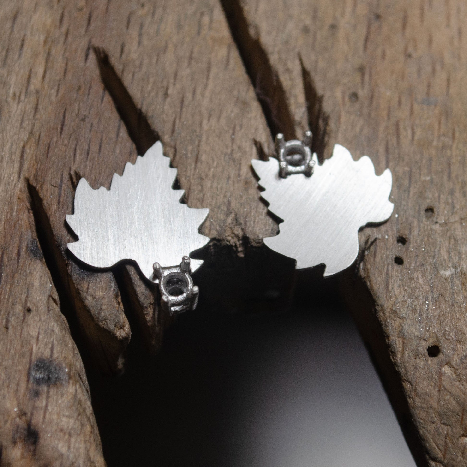 vue rapprochée d'une paire de boucles d'oreilles en argent en forme de feuille en cours de fabrication sur une surface en bois