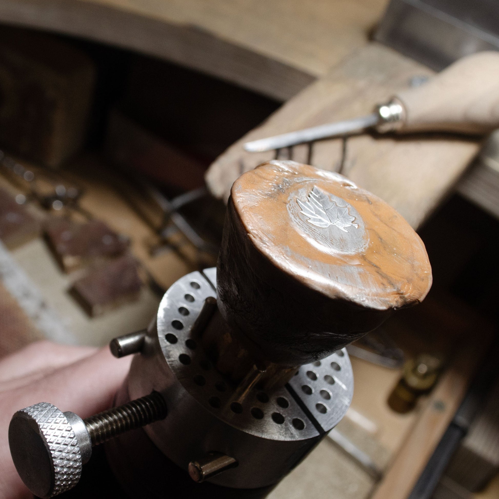 Poignée en bois avec une piece de bijous en argent tenue par une main sur un établi.