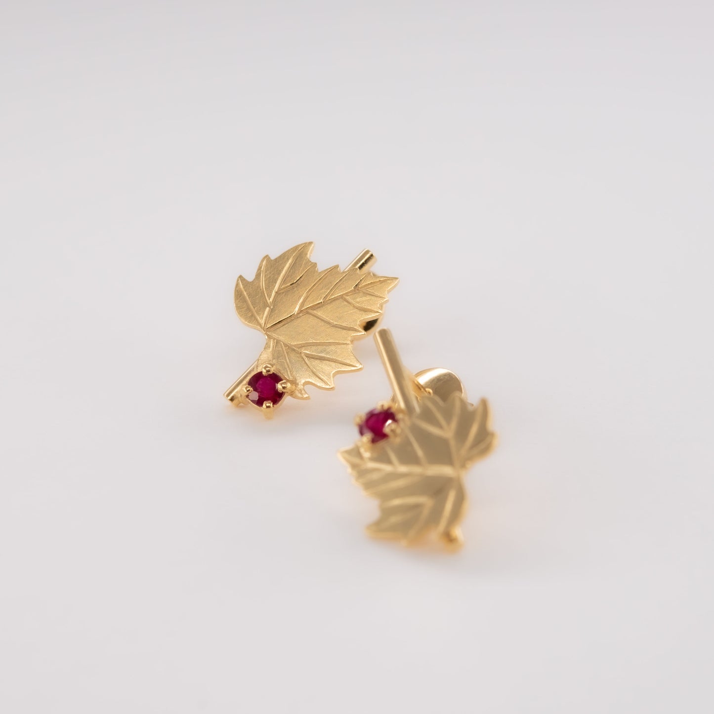 Boucles d'oreilles en forme de feuilles en or avec des pierres précieuses rouges rubis sur un fond blanc clair