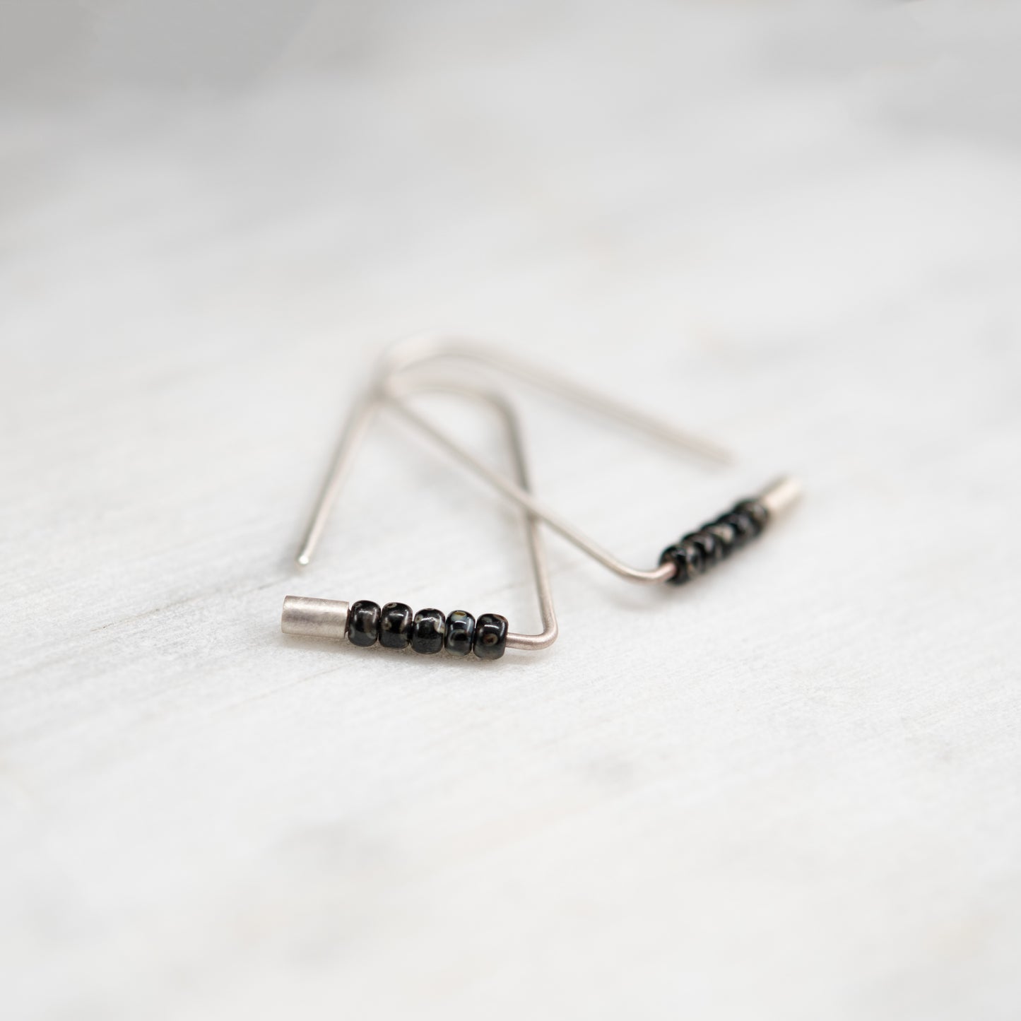 Boucles d’oreilles triangulaires faites main en argent avec perles Miyuki, photographiées en gros plan.