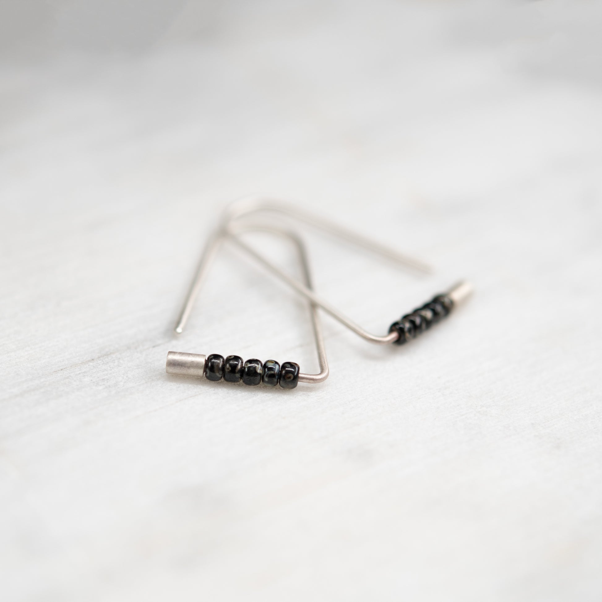 Boucles d’oreilles triangulaires faites main en argent avec perles Miyuki, photographiées en gros plan.