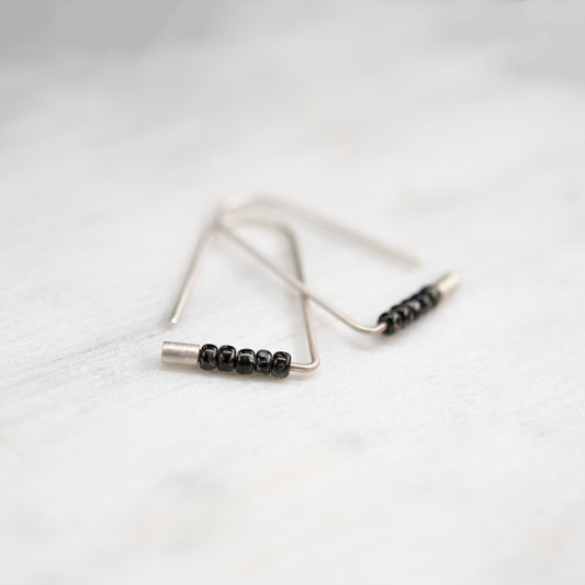 Boucles d’oreilles triangulaires faites main en argent avec perles Miyuki, photographiées en gros plan.